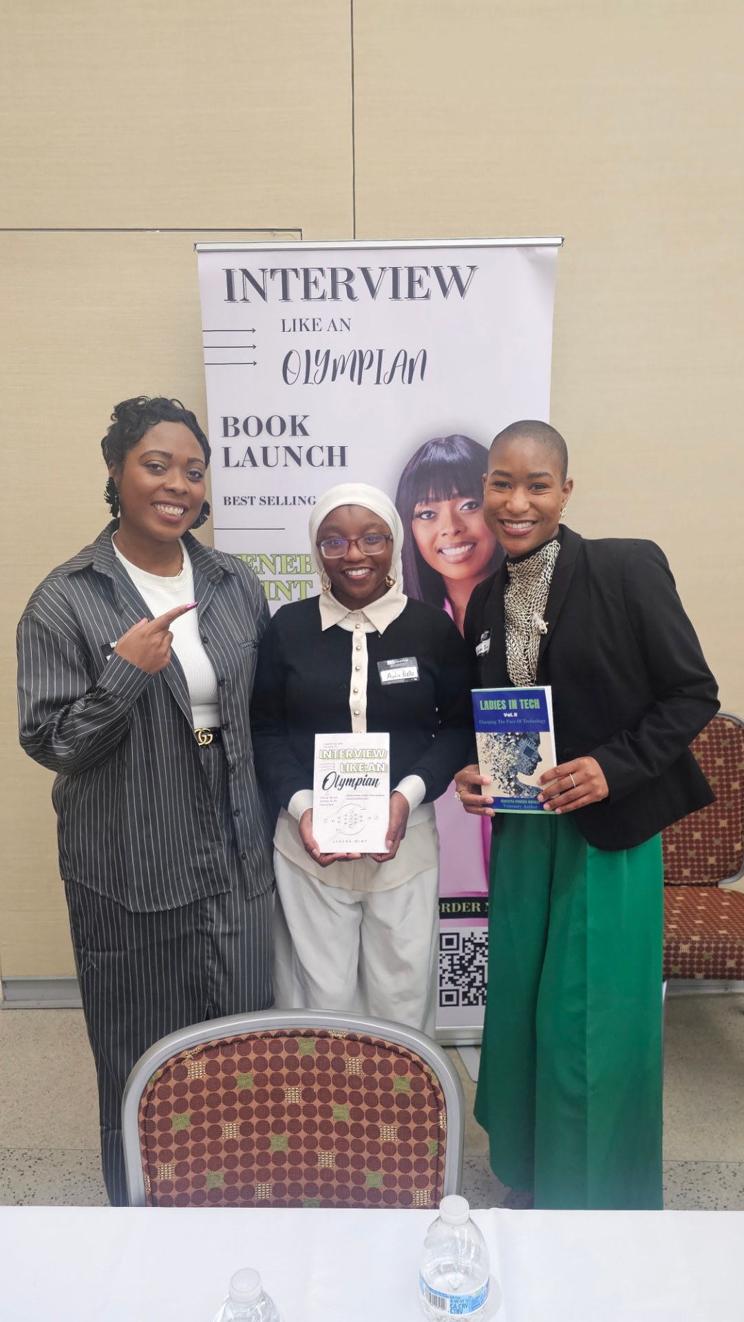 Jeneba Wint with two authors holding their books in front of the book launch banner.