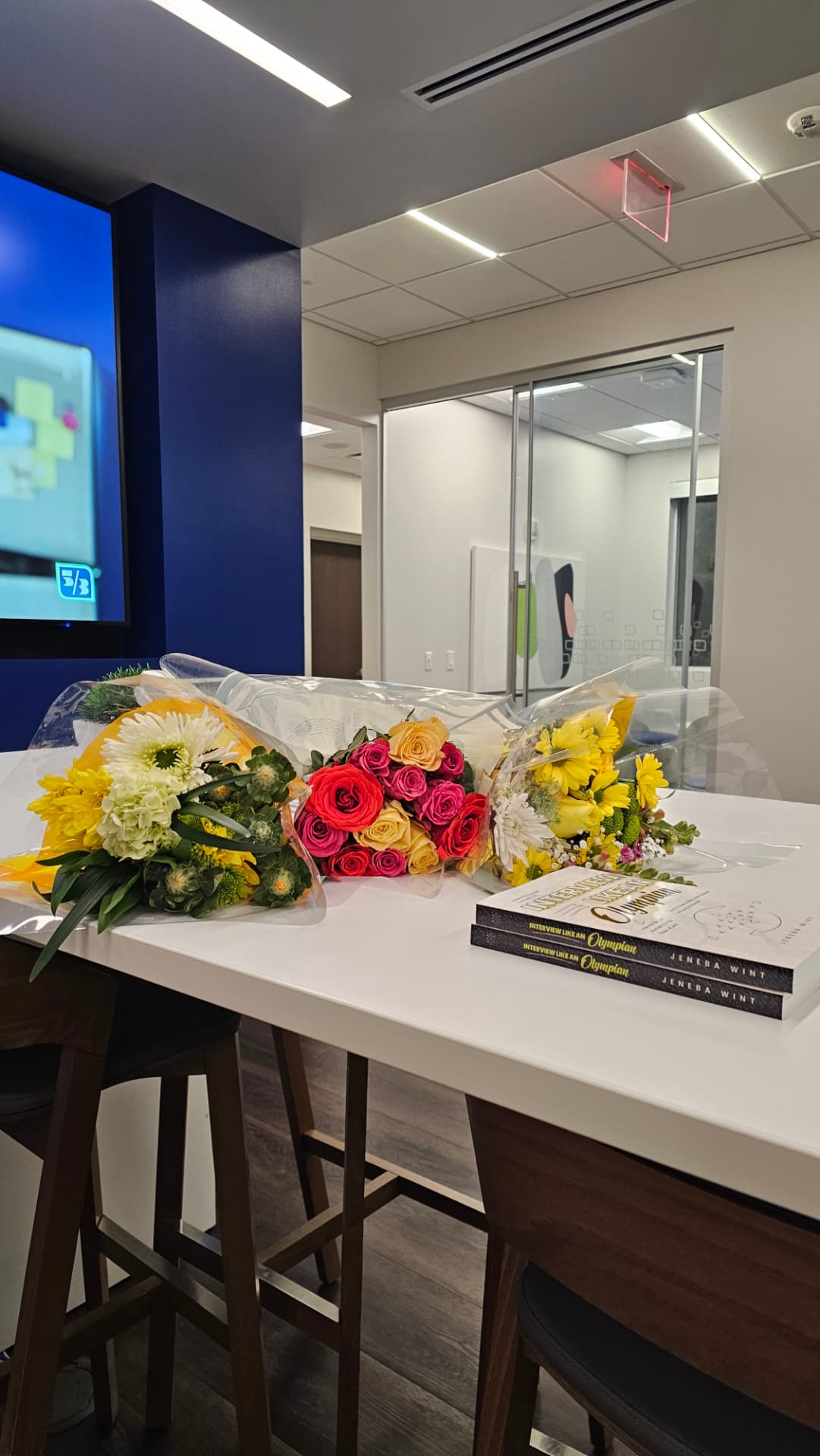 Copies of Interview Like an Olympian beside colorful flower bouquets at a book celebration.